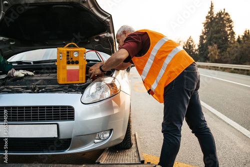 Two road assistant workers in towing service trying to start car engine with jump starter and energy station with air compressor. Roadside assistance concept. photo