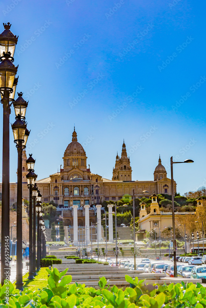 Avenue with straight post lamps, cars, the four pillars of the magic fountain of Montjuic and the National Museum of Art of Catalonia in the background, sunny day in the city of Barcelona Spain
