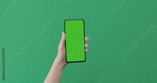 Young female hand hold smartphone with green screen on green background