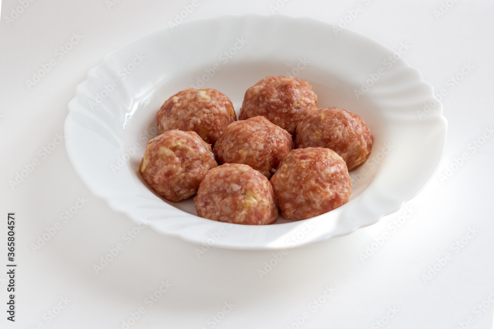 Raw meat balls with rice, spices, sauce, finely chopped cabbage are ready for cooking. A few raw noisettes lie on a white plate. Raw meat balls with rice, spices, sauce, finely chopped cabbage are ready for cooking. A few raw noisettes lie on a white plate.