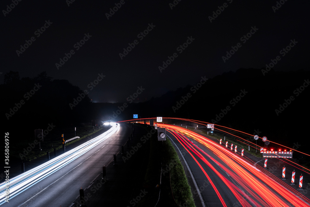 Langzeitbelichtung von einer Autobahnbrücke auf die Baustelle bei Nacht. Stadtlichter, Sterne auf dem Himmel.