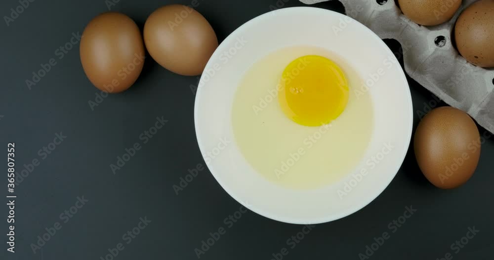 Truck shot of human hand breaking raw chicken egg into the white bowl on black background Truck shot of human hand breaking raw chicken egg into the white bowl on black background