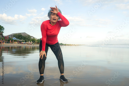 portrait of fit and tired middle aged woman after beach running workout - 40s or 50s attractive mature lady with grey hair breathing exhausted after jogging