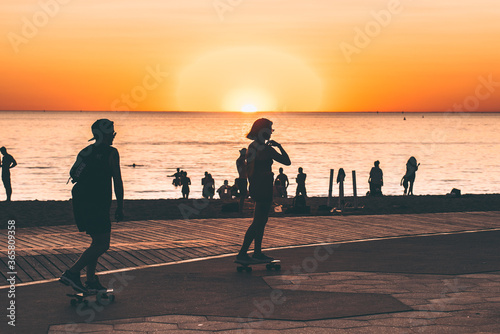 Skateboarders along beach at sunset 
