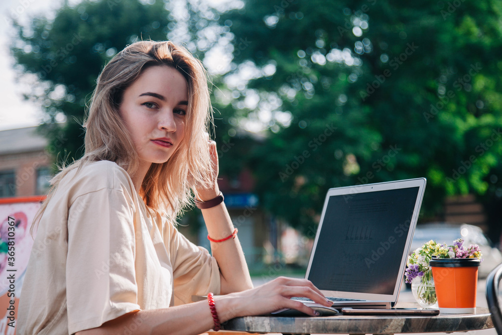 A young girl on a summer playground of a coffee shop works behind a laptop and drinks coffee from a disposable cup A young girl on a summer playground of a coffee shop works behind a laptop and drinks coffee from a disposable cup