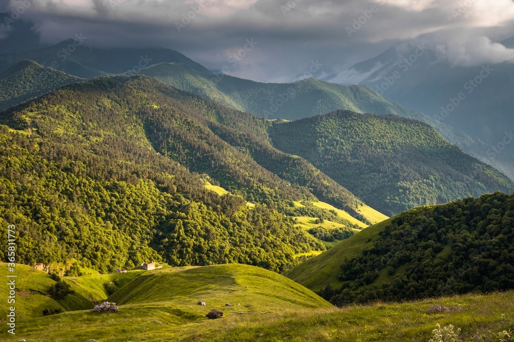 Terrific view of the green Caucasus mountains under heavy clouds and slopes covered with endless forests. Russia.