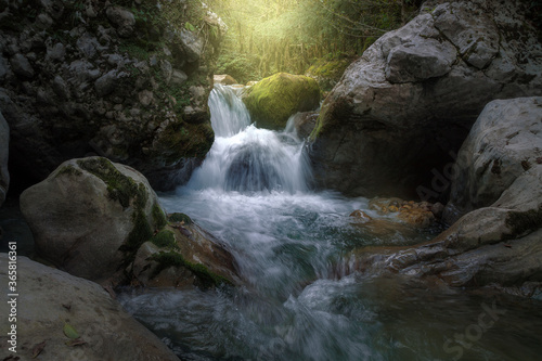 sunlight illuminates a waterfall among huge rocks in the forest