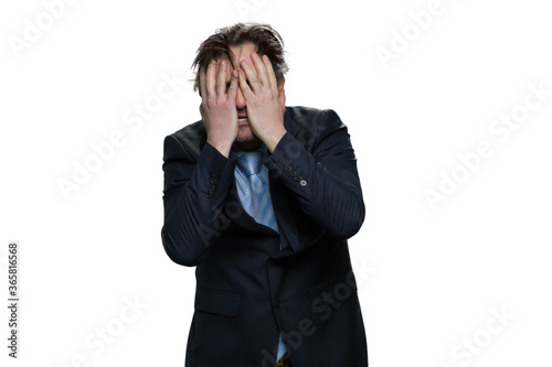 Middle-aged businessman covering his eyes with his hands in desperation. Exhausted man in suit isolated on white background.