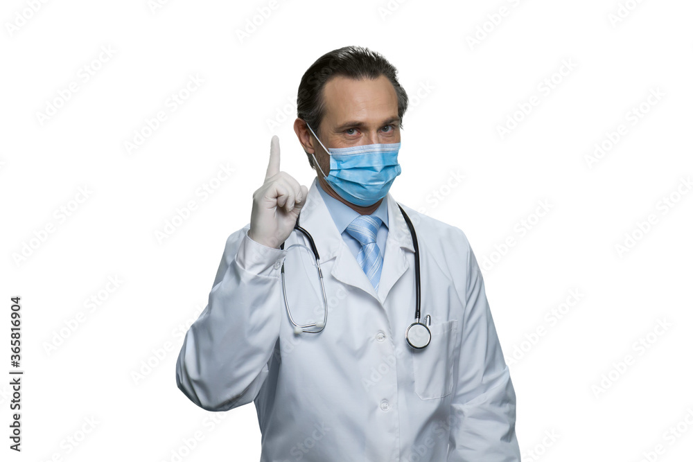 Middle-aged doctor in respirator mask with raised forefinger. Portrait of confident doctor with stethoscope isolated on white background.