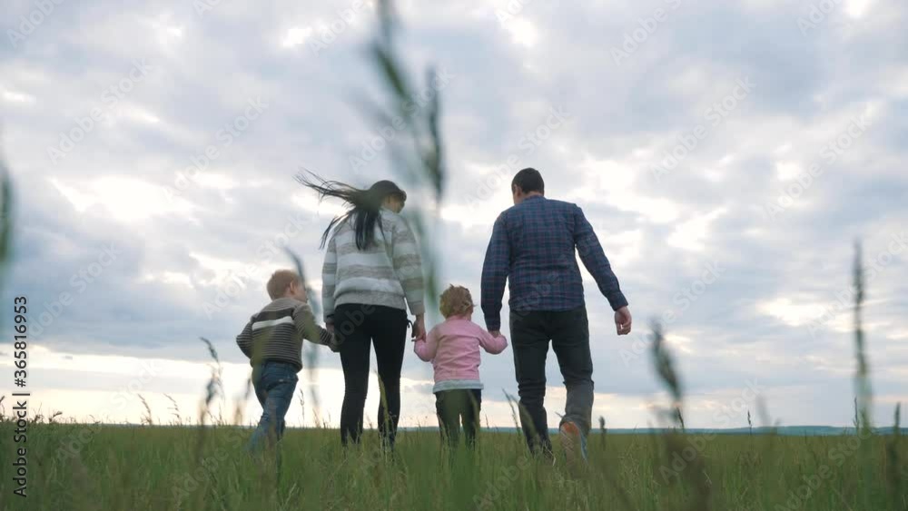 Young happy parents with children together, holding hands, walking on the green grass in the fresh air. A happy family has a fun weekend and socialize with each other.