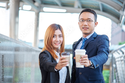 Young Asian Business people smiling and Relax holding a cup of coffee before go to work. Couple lover enjoy drinking coffee together in modern city. Business people holding cup of coffee at office