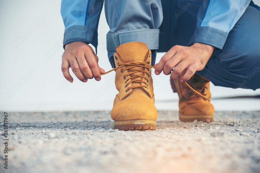 Man kneel down and tie shoes industry boots for worker. Close up shot of  man hands