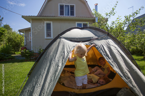 Three pretty preschool girls having fun outside in front of their country house in sunny summer day. They are playing in touristic tent. Staycation concept. New normal photo