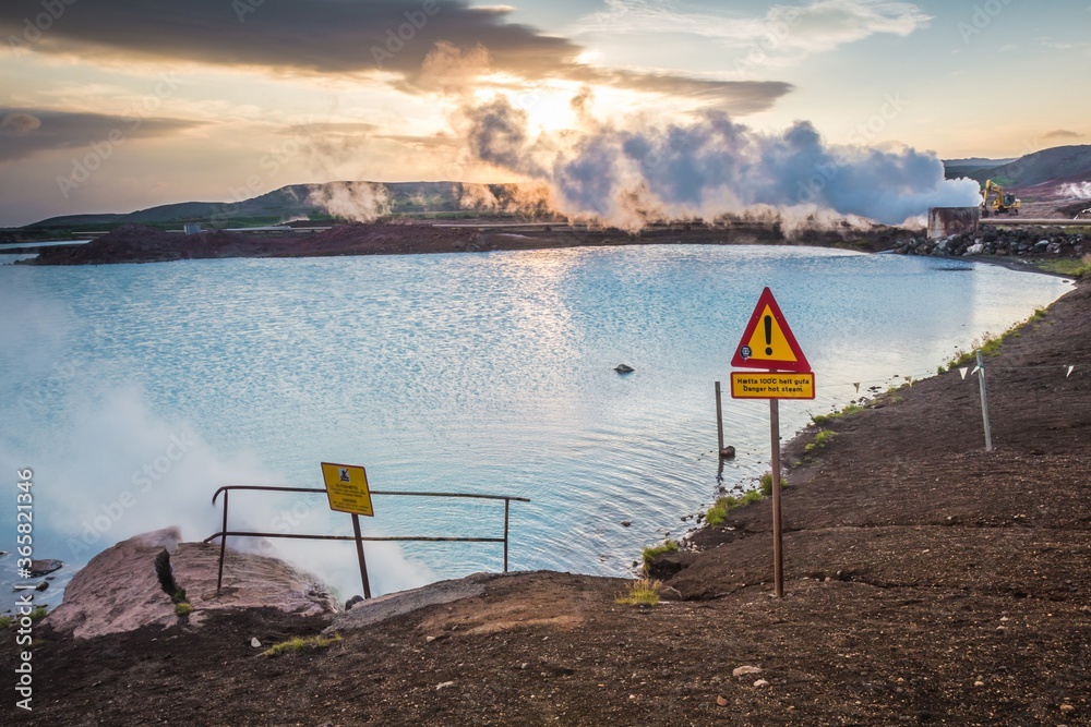Picturesque blue  hot geothermal lake in the evening. Warning signs on the foreground. Steam goes from geothermal power station in Iceland. Sigh 