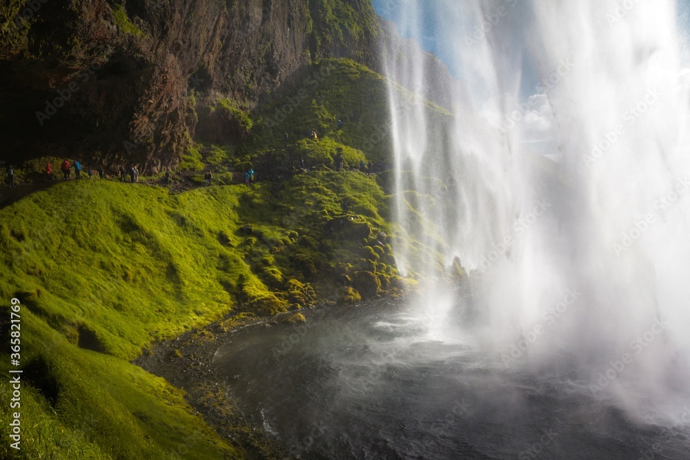 Amazing waterfall Seljalandsfoss in Iceland and tourist near it. The waterfall drops 60m (197 ft) and is part of the Seljalands River. Visitors can walk behind the falls into a small cave.