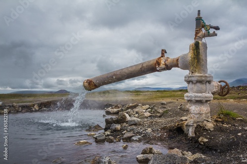 End of a rusty pipeline with hot geothermal water flowing into the pond in Iceland.