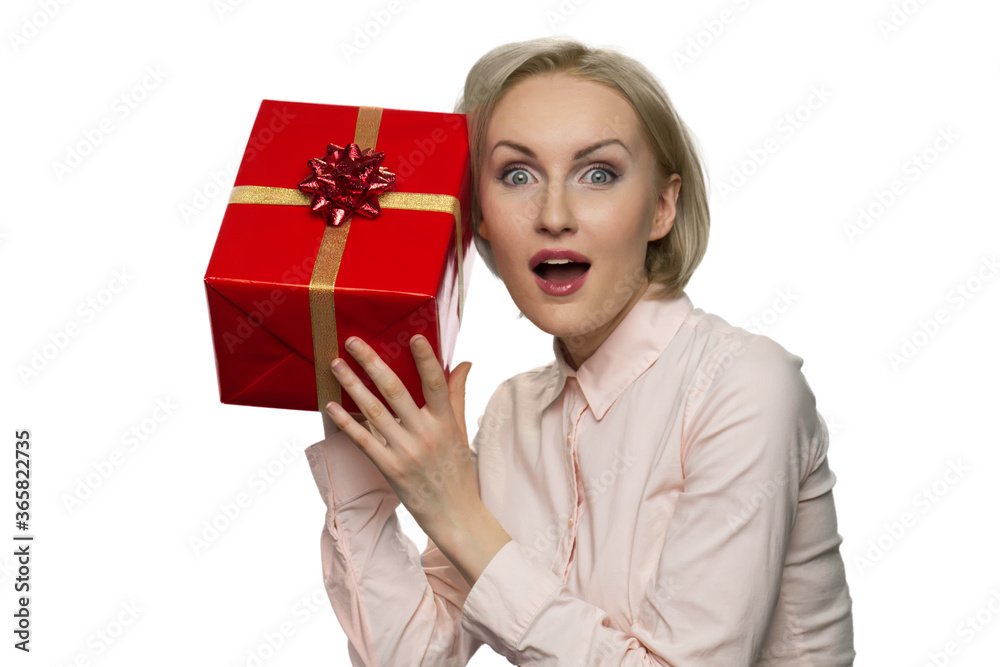 Suprised woman with opened mouth putting her ear to the present in red paper. Nosy impatient girl in white shirt trying to guess inside gift box. Suprised woman with opened mouth putting her ear to the present in red paper. Nosy impatient girl in white shirt trying to guess inside gift box.