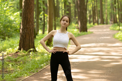 Beauty, health, fitness. Girl warming up in the park before jogging, doing exercises in nature