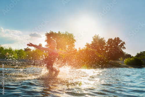 Happy child playing in the water at sunset. Summer vacation and healthy lifestyle concept. © Andrii