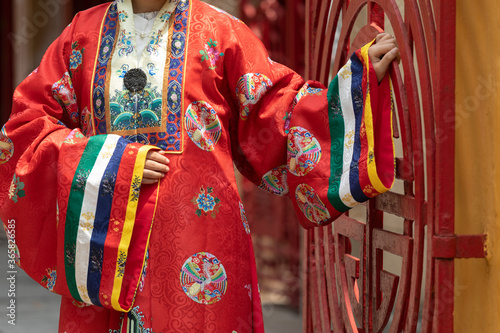 detail of traditional Vietnamese red silk robes. Model is standing next to a red gate. These robes were worn by royalty