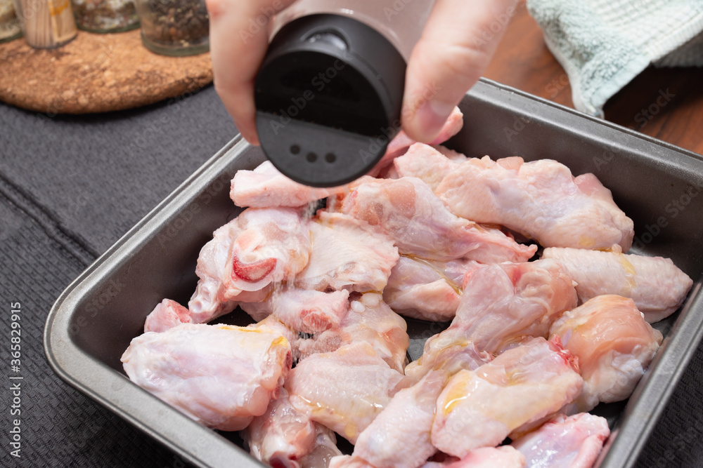 Cooking chicken wings. Male hand adds salt and seasoning before going to the oven
