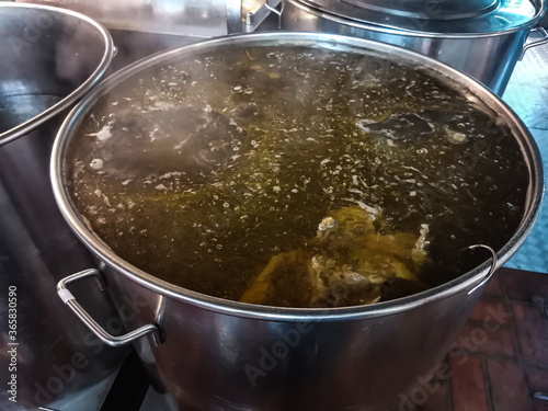 A huge industrial metal pan with boiling beef broth. Street Vietnamese cafe, making traditional Asian soups. The main ingredient for pho bo soup.
