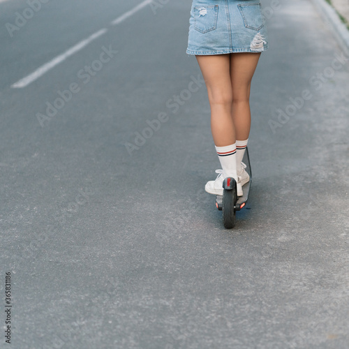 Young beautiful girl riding an electric scooter in the summer on the street