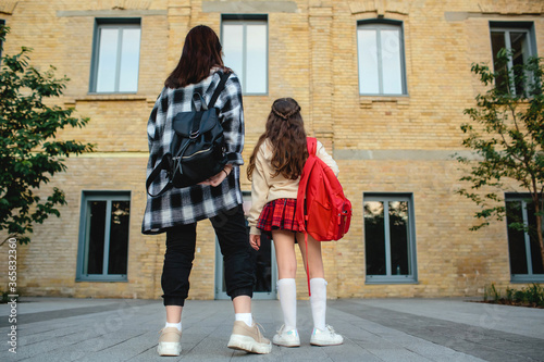 Back to school concept. Two schoolgirls in uniform with backpacks against the school background, view from back. © Hanna