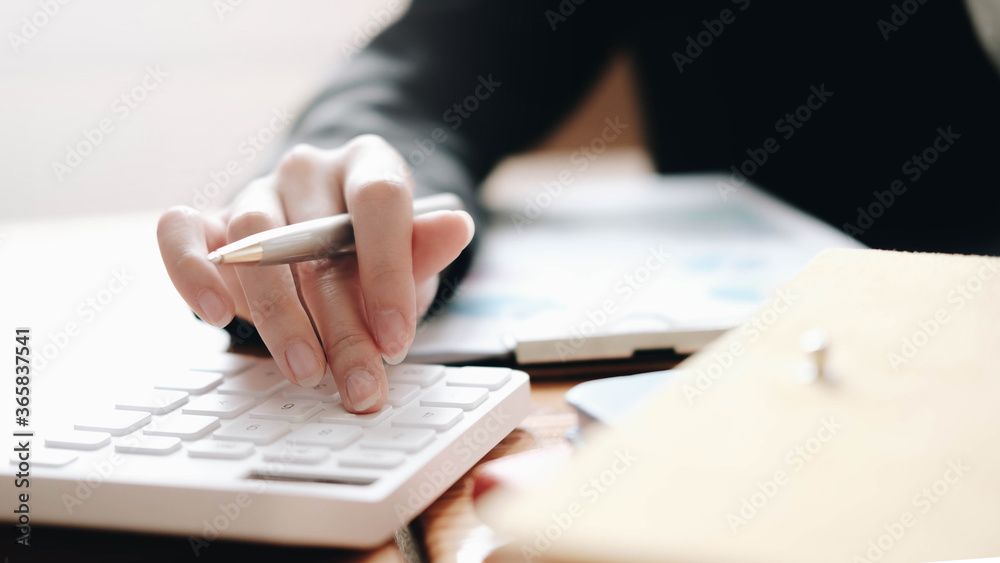 Close up Business woman using calculator and laptop for do math finance on wooden desk in office and business working background tax accounting statistics and analytic research concept Close up Business woman using calculator and laptop for do math finance on wooden desk in office and business working background tax accounting statistics and analytic research concept