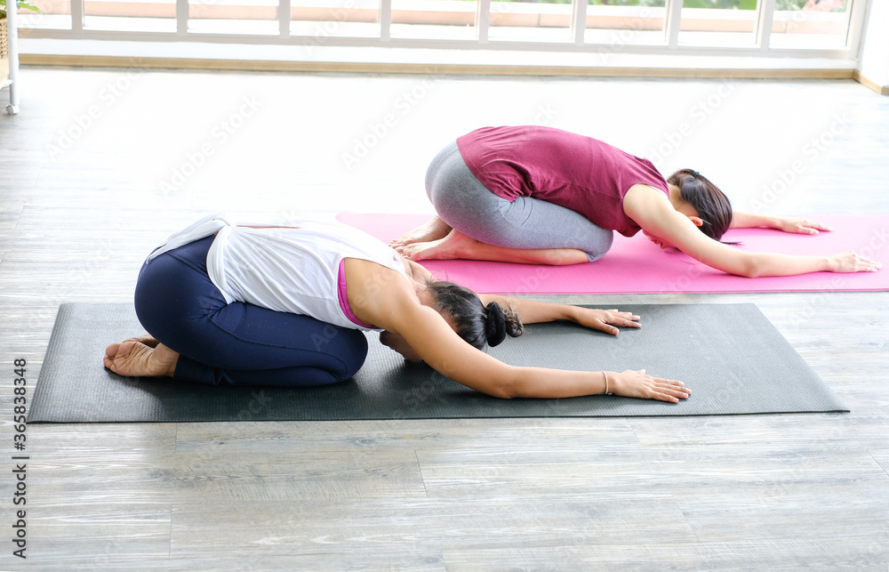 2 Asian woman practicing yoga together relax in Hatha yoga asana Balasana , child's pose resting position or counter asana on yoga mat at home,working out,concept of healthy life and natural balance 2 Asian woman practicing yoga together relax in Hatha yoga asana Balasana , child's pose resting position or counter asana on yoga mat at home,working out,concept of healthy life and natural balance