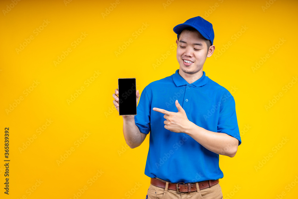 Asian delivery man pointer to application on mobile phone over yellow isolate background. Work from home and delivery concept.