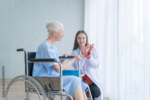 Happy woman doctor talking to disabled old female senior elderly patient on wheelchair in hospital ward room in medical and healthcare treatment concept. Caucasian white people. photo