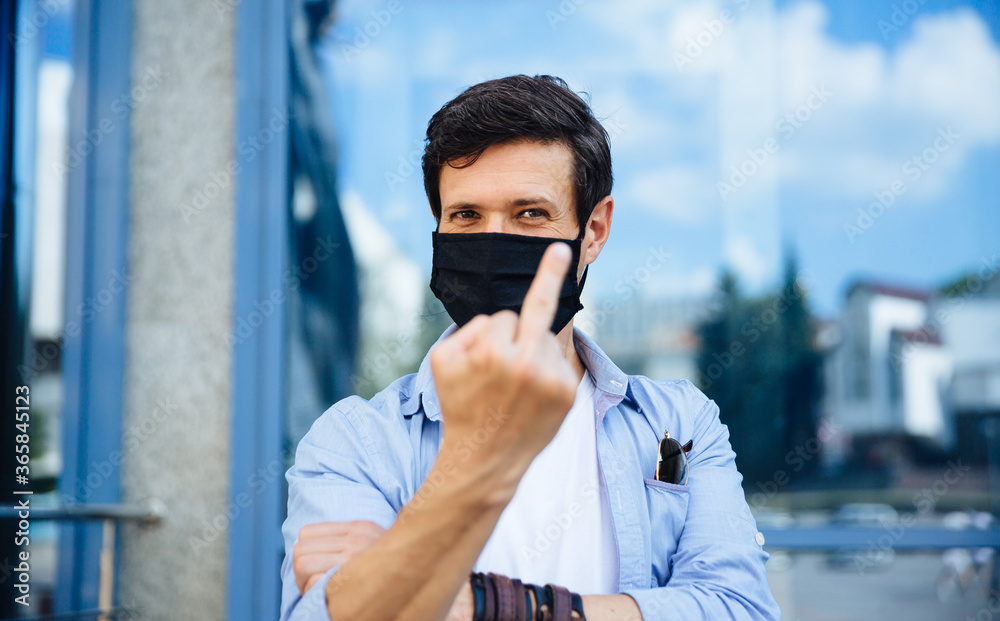 Portrait of optimistic positive man in surgical mask showing middle finger to covid Portrait of optimistic positive man in surgical mask showing middle finger to covid