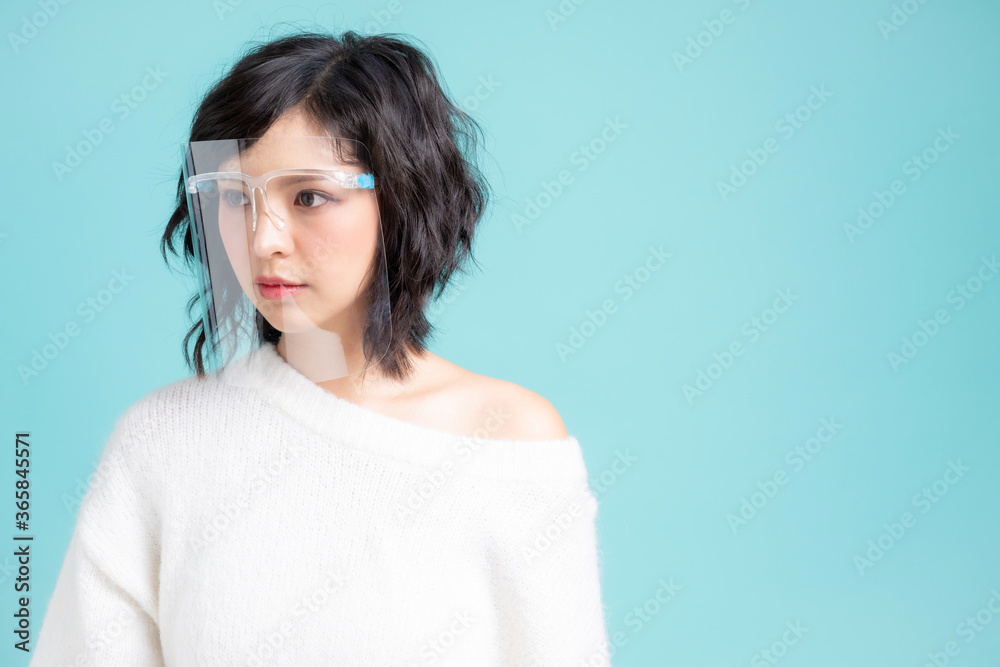 Young Asian woman wearing a face shield. Isolated image over light blue background. Young Asian woman wearing a face shield. Isolated image over light blue background.
