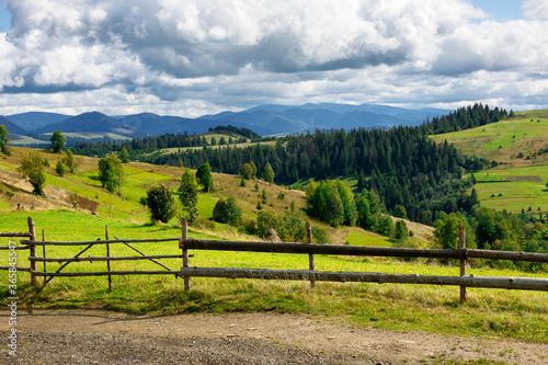 fence on the hill in rural area. early autumn scenery in carpathian mountains. sunny weather with clouds on the sky. hills rolling in tho the distant mountain ridge
