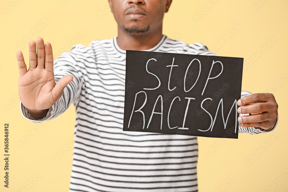 Sad African-American man with poster showing stop gesture on color background. Stop racism Sad African-American man with poster showing stop gesture on color background. Stop racism