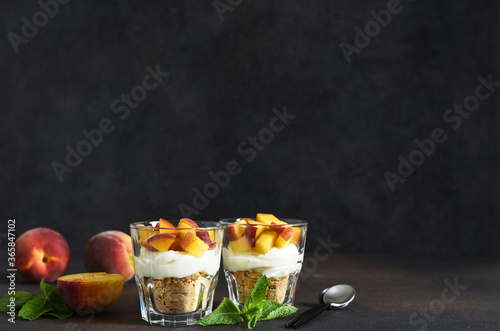 Cheesecake with peach and cookies in a glass on a dark, concrete background. Cheesecake without baking. Dessert. New York.