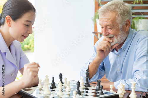 Senior retirement man playing chess with nurse at home photo