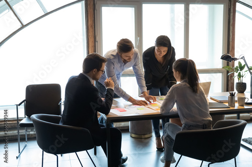 Concentrated diverse businesspeople gather at desk in office work together analyzing company paperwork  colleagues coworkers brainstorm discuss financial documents at meeting  cooperation concept