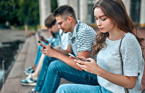 A group of students sit on the steps outside the campus and use their smartphones.