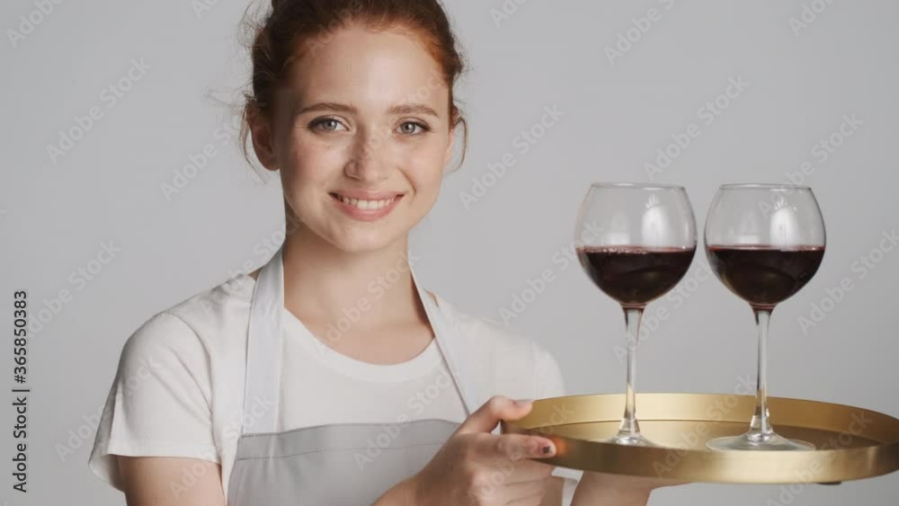 Close up beautiful confident waitress in apron holding tray with glasses of red wine over white background Close up beautiful confident waitress in apron holding tray with glasses of red wine over white background