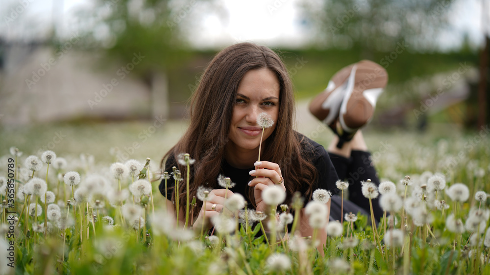 Beautiful smiling girl with long brown hair lying in dandelion field Beautiful smiling girl with long brown hair lying in dandelion field