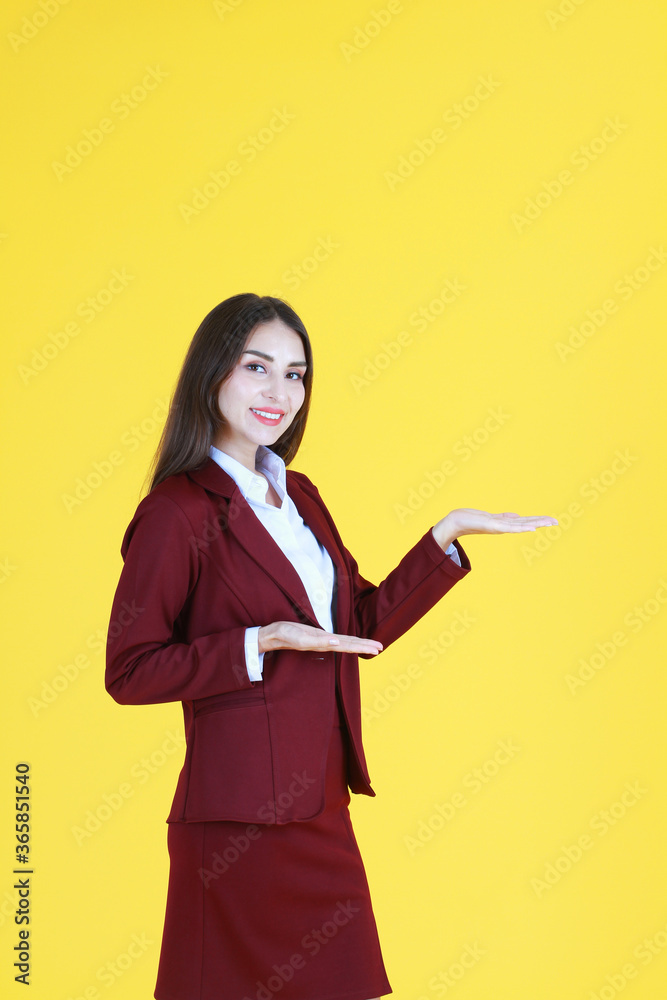 Smart Caucasian woman in red suit smiling and her hand open for present isolated on yellow background. Copy space Smart Caucasian woman in red suit smiling and her hand open for present isolated on yellow background. Copy space