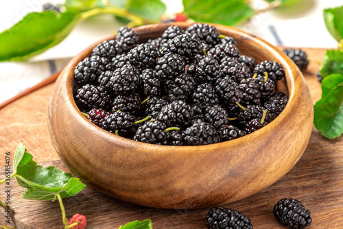 Fresh black mulberry in a wooden bowl and leaves on the table. Mulberry close-up.