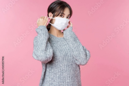 Young Asian girl taking off her face mask image isolated on pink studio background.
