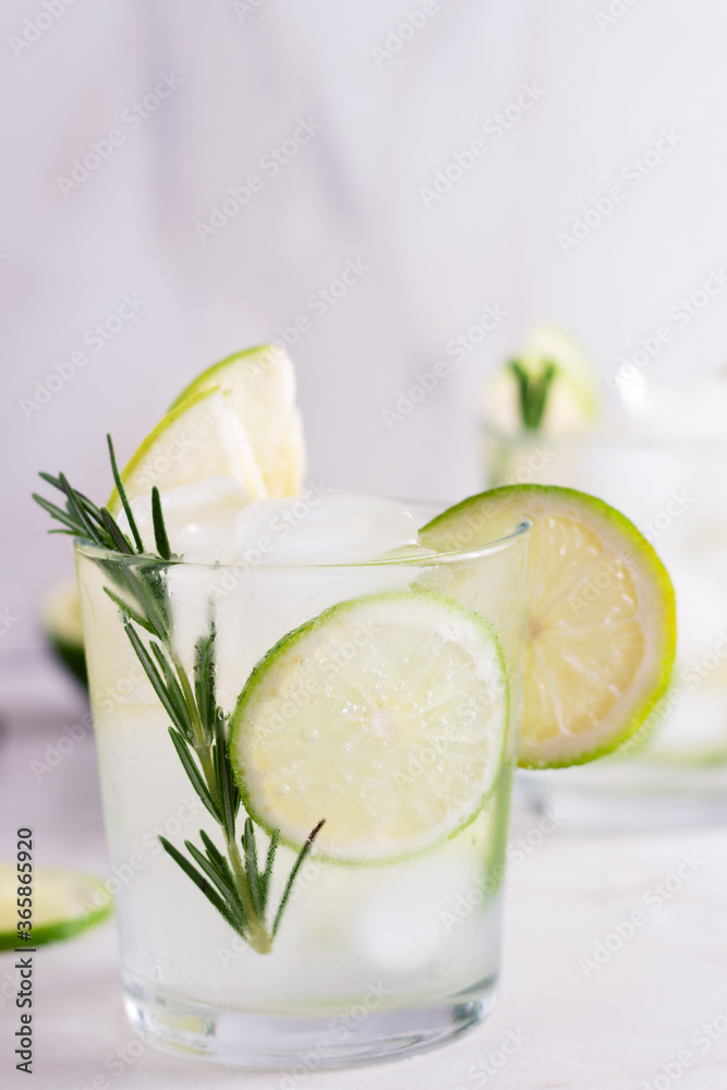 Fototapeta premium Cold fresh summer cocktail with lime, mint,rosemary and ice in glasses on a light background