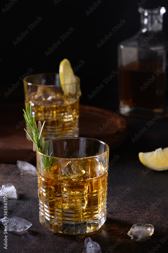 Three glasses of cold whiskey with rosemary, lemon peels on dark brown background. Vertical. Close up. Three glasses of cold whiskey with rosemary, lemon peels on dark brown background. Vertical. Close up.