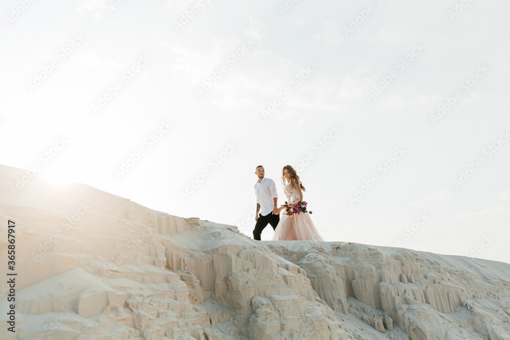 Love Story of a beautiful couple in a pink wedding luxury dress with a bouquet in the Sahara desert, sand, dunes