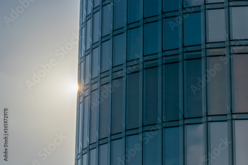 Wallpaper Mural The sun peeps out from behind a round skyscraper on a blue sky background Torontodigital.ca