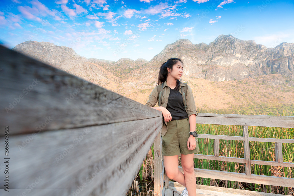 Naklejka premium Freedom traveler woman standing with raised arms and enjoying a beautiful nature and cheering young woman backpacker at sunrise seaside mountain peak